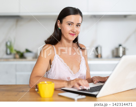 Adult woman working on laptop in kitchen Adult woman working on laptop in kitchen 142314471