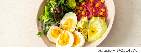 A bowl holds beet hummus topped with chickpeas, fresh broccoli, and microgreens salad alongside slices of avocado and boiled eggs. This meal is nutritious and filling, banner A bowl holds beet hummus topped with chickpeas, fresh broccoli, and microgreens salad alongside slices of avocado and boiled eggs. This meal is nutritious and filling, banner 142314578