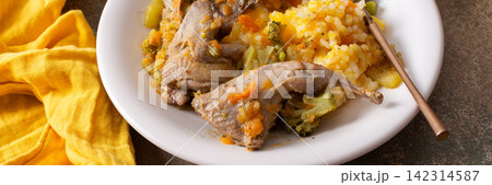 A plate holds rice and stewed quail, showing a mix of vegetables. The meal is placed on a plain surface, ready to be enjoyed for breakfast or lunch, banner 142314587