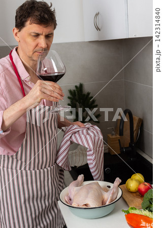 A man is in a kitchen preparing a pre-Christmas dinner. He is focused on baking chicken with potatoes while serving himself a glass of red wine A man is in a kitchen preparing a pre-Christmas dinner. He is focused on baking chicken with potatoes while serving himself a glass of red wine 142314840