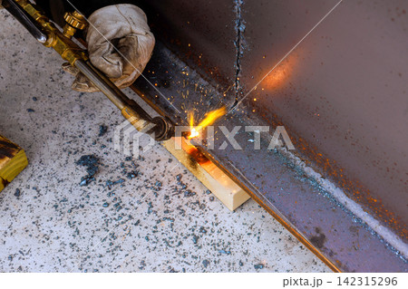 Worker is welding metal pieces together in workshop sparks are flying as torch ignites metal. Worker is welding metal pieces together in workshop sparks are flying as torch ignites metal. 142315296