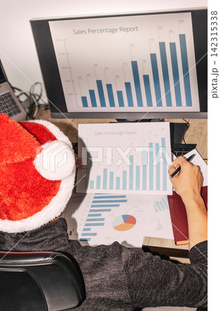 Santa-hatted individual analyzes bar graphs on desk Santa-hatted individual analyzes bar graphs on desk 142315338