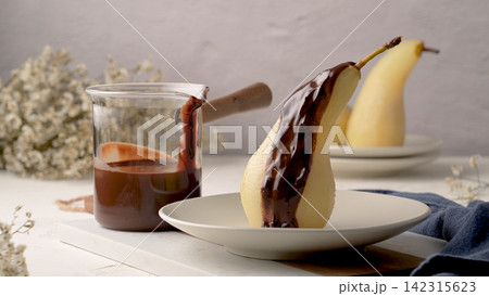 Poached pear drizzled with rich chocolate sauce on a white plate Poached pear drizzled with rich chocolate sauce on a white plate 142315623
