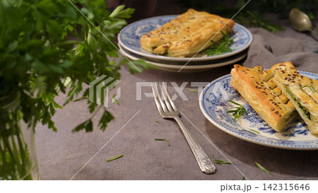 Flaky puff pastry stuffed with savory green filling on vintage patterned plates Flaky puff pastry stuffed with savory green filling on vintage patterned plates 142315646