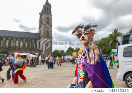 Masked therian girl in colorful rainbow cape poses during CSD celebration in Magdeburg, Germany, with cathedral behind. Scene reflects youth subculture, fandom, identity, pride, creativity, community Masked therian girl in colorful rainbow cape poses during CSD celebration in Magdeburg, Germany, with cathedral behind. Scene reflects youth subculture, fandom, identity, pride, creativity, community 142315836