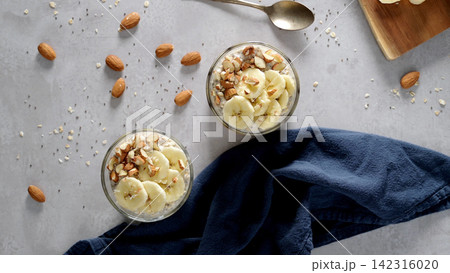 Overnight oats with banana slices and almonds in glass jars 142316020