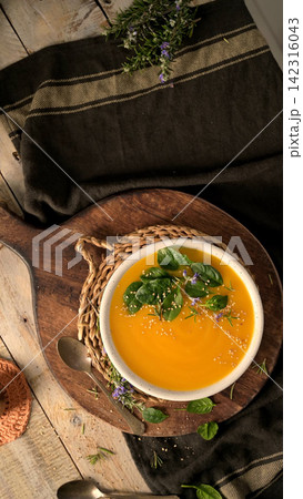 Creamy pumpkin soup served in a white bowl with spinach leaves and sesame seeds 142316043