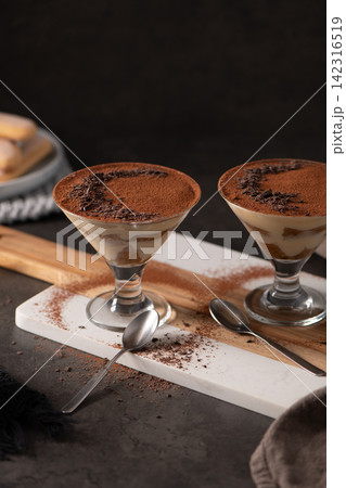 Two Tiramisu Desserts Served in stemmed cocktail Glasses on a Marble and Wood Board Two Tiramisu Desserts Served in stemmed cocktail Glasses on a Marble and Wood Board 142316519