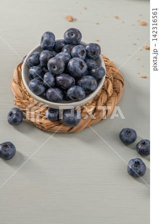 Fresh blueberries in a small bowl on a woven mat 142316561