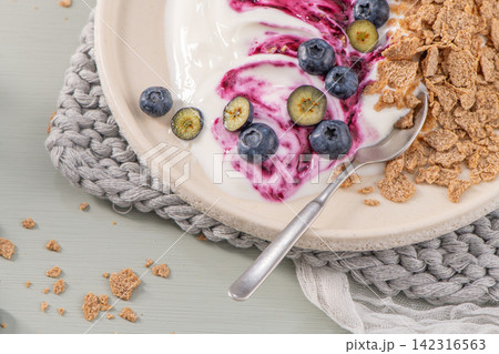 Healthy breakfast bowl with creamy yogurt, blueberry swirl, fresh berries, and whole-grain cereal flakes 142316563