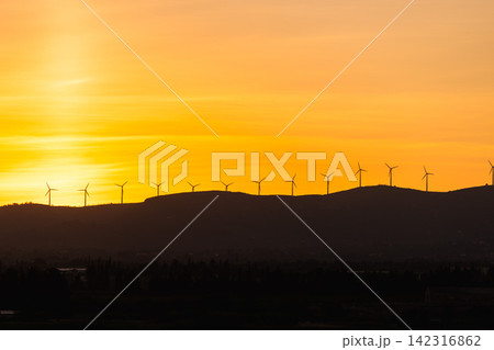 Wind turbines on mountain ridge at sunset representing renewable energy generation and sustainable electricity production 142316862
