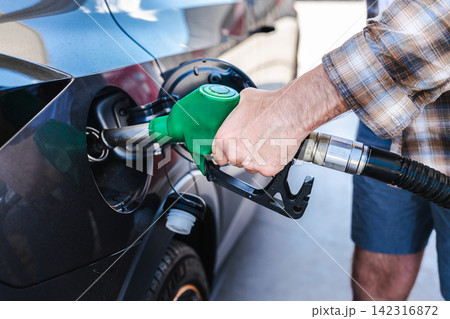 Man refueling modern vehicle with green gasoline nozzle at fuel station 142316872