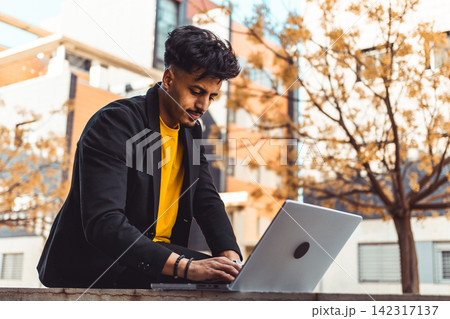 Moroccan man working on laptop outdoors in city Moroccan man working on laptop outdoors in city 142317137