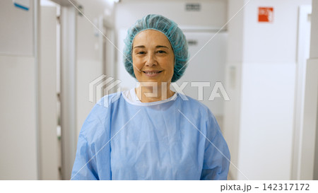 Female surgeon smiling wearing scrubs in hospital hallway Female surgeon smiling wearing scrubs in hospital hallway 142317172