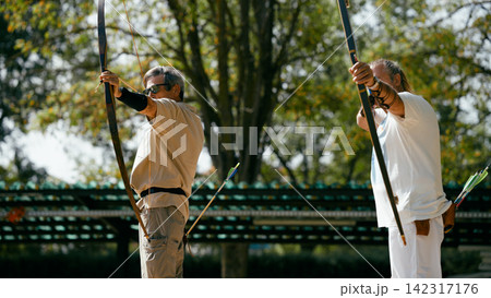 Senior men practicing archery, aiming for goals outdoors 142317176
