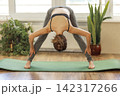 Woman practices yoga in a room with plants and large windows during daytime 142317266