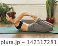 Woman practicing yoga in a home setting during the day with plants in the background 142317281