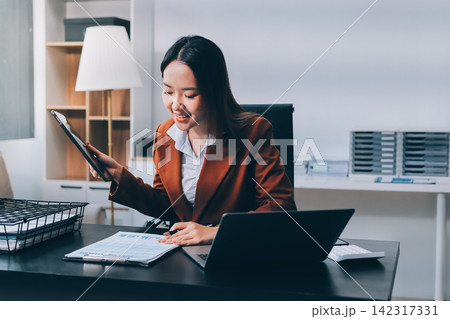Asian businesswoman using calculator and working on laptop at modern office 142317331