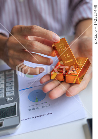 Physical gold bars on investor's hand at office desk. Concept for secure financial investment and wealth preservation. Physical gold bars on investor's hand at office desk. Concept for secure financial investment and wealth preservation. 142317449