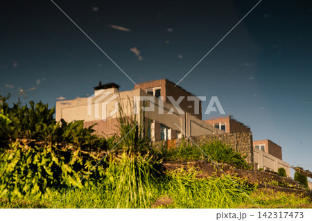 Modern residential buildings rise above lush wild vegetation on a sunny hillside. Warm evening light highlights the architecture, greenery and quiet suburban setting, creating a serene urban landscape 142317473