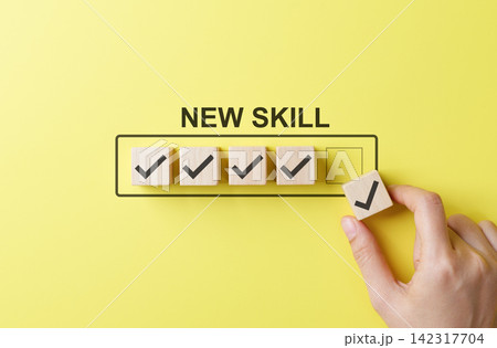 New skill development and learning progress concept with hand placing checkmark block on checklist against yellow background, symbolizing self-improvement, upskilling, goal setting, and career growth. 142317704