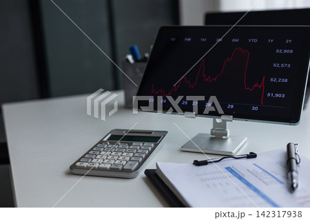 A digital tablet showing a stock market price chart with a red downward trend line on desk in bright office. A digital tablet showing a stock market price chart with a red downward trend line on desk in bright office. 142317938