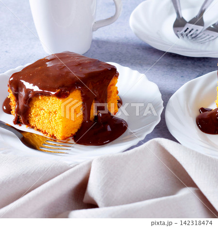 Slice of Brazilian carrot cake topped with creamy, glossy chocolate on a white plate, accompanied by a cloth napkin Slice of Brazilian carrot cake topped with creamy, glossy chocolate on a white plate, accompanied by a cloth napkin 142318474