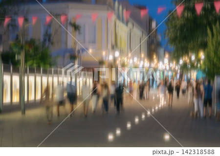 Blurred Crowd Walking on Illuminated City Street at Night. Anonymous people walking along illuminated pedestrian street at night, intentional motion blur. Urban evening expressing movement, city life Blurred Crowd Walking on Illuminated City Street at Night. Anonymous people walking along illuminated pedestrian street at night, intentional motion blur. Urban evening expressing movement, city life 142318588