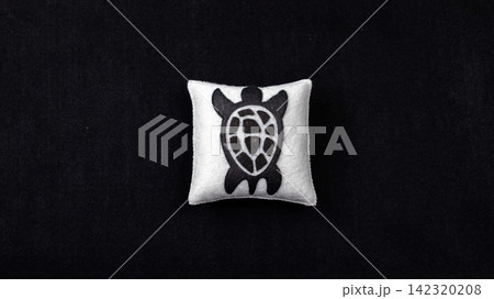Handmade felt sea turtle ornament on white cushion against black background 142320208