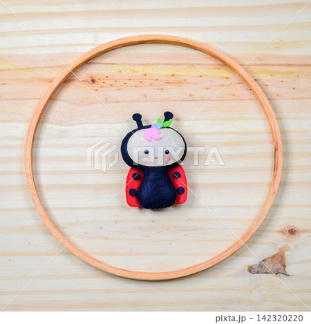 Handmade felt ladybug decor arranged inside a circular wooden ring on a light wooden background 142320220