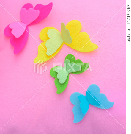Colorful handmade felt butterflies in pink, yellow, green, and blue arranged on a soft pink pillow background 142320267