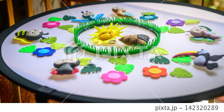 Colorful handmade nursery mobile with colorful felt animals, flowers, leaves, grass, and a smiling sun arranged on a white surface Colorful handmade nursery mobile with colorful felt animals, flowers, leaves, grass, and a smiling sun arranged on a white surface 142320289