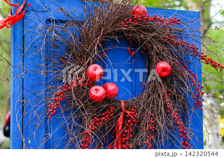 Handmade rustic wreath made of dry twigs red apples and berries hanging on vintage blue wooden door with copy space area. Handmade rustic wreath made of dry twigs red apples and berries hanging on vintage blue wooden door with copy space area. 142320544