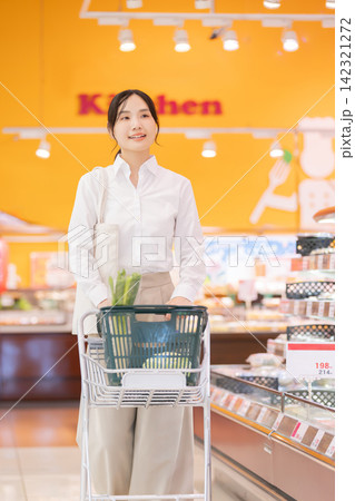 スーパーの食品売り場でショッピングカートを押して買い物をする笑顔の若い女性 142321272
