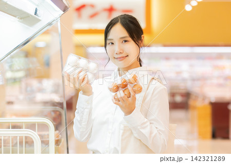 スーパーの卵売り場で白い卵と茶色い卵を比較して選ぶ若い女性 スーパーの卵売り場で白い卵と茶色い卵を比較して選ぶ若い女性 142321289