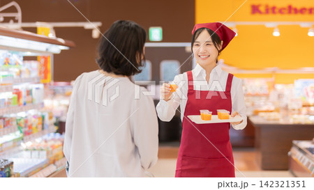 スーパーマーケットで女性客に試飲ドリンクを勧める笑顔の女性スタッフ スーパーマーケットで女性客に試飲ドリンクを勧める笑顔の女性スタッフ 142321351