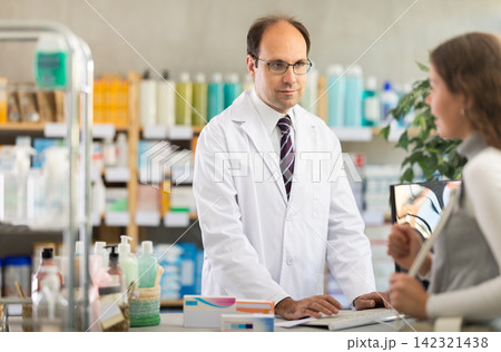 Pharmacist searches for medicine on computer for female buyer 142321438