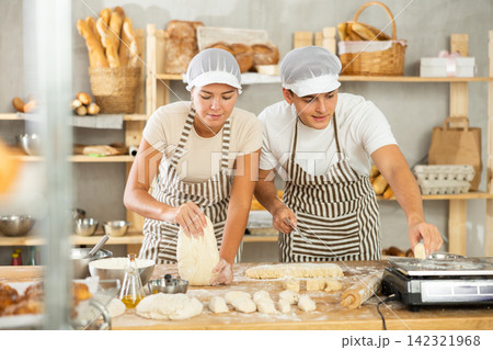 Girl and guy bakers cut small pieces of dough from large lump and put them on scales. 142321968