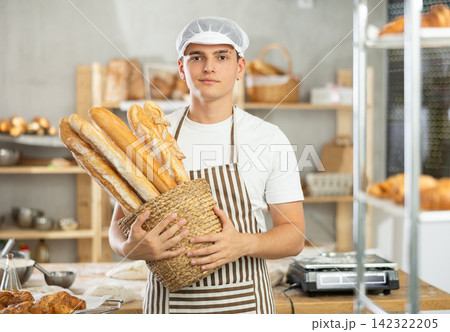Happy male baker posing with basket of freshly baked baguettes in bakery, demonstrating concept of food industry and baker profession Happy male baker posing with basket of freshly baked baguettes in bakery, demonstrating concept of food industry and baker profession 142322205