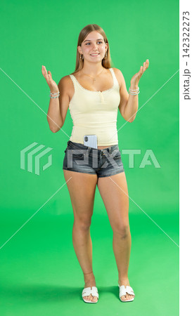 Portrait of teenage girl in black denim shorts expressing happy emotions on green background Portrait of teenage girl in black denim shorts expressing happy emotions on green background 142322273