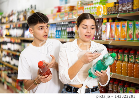 Young man and woman searching on internet contents of soft drinks together in supermarket Young man and woman searching on internet contents of soft drinks together in supermarket 142322293
