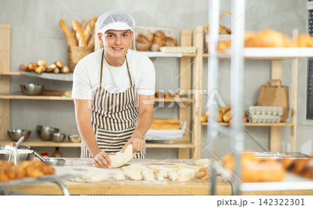 Young male baker kneading dough in bakery 142322301