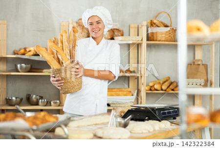 Young woman are standing in kitchen with basket of finished products baguettes Young woman are standing in kitchen with basket of finished products baguettes 142322384