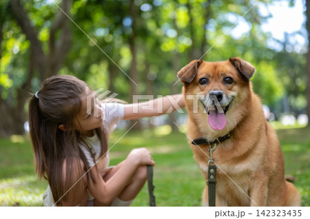 Young girl owner smiling beside her dog while gently stroking its head in the park. 142323435
