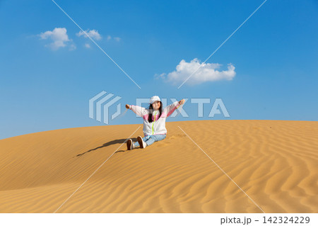 A cheerful young girl sits on the warm sand with open arms, enjoying her vacation in a beautiful sunny desert. A cheerful young girl sits on the warm sand with open arms, enjoying her vacation in a beautiful sunny desert. 142324229