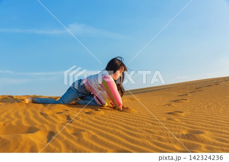 A little girl playing happily on the ground in the desert; the concept of a happy holiday trip. 142324236