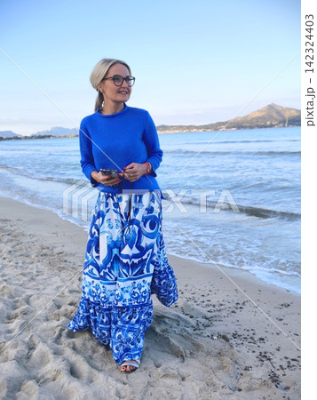Smiling woman in blue dress on sandy beach at sunset 142324403
