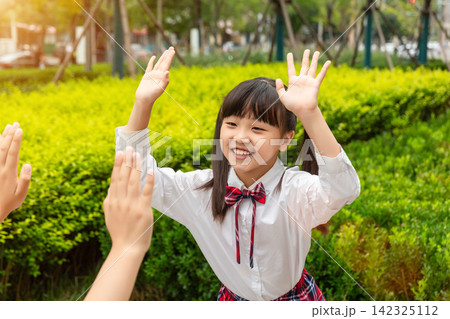A happy young schoolgirl smiling and giving a high five to her friend outdoors during recess. 142325112