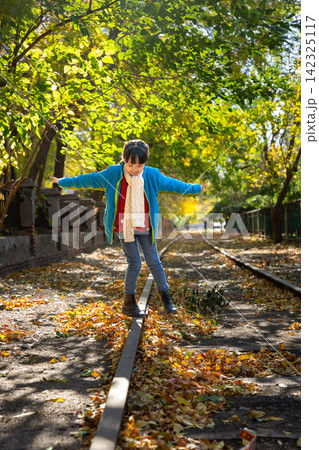 A joyful child standing on an autumn railway track with arms wide open under beautiful green and yellow trees. A joyful child standing on an autumn railway track with arms wide open under beautiful green and yellow trees. 142325117