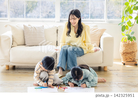 リビングでお絵かきをする子供たちを見守る母親 リビングでお絵かきをする子供たちを見守る母親 142325951
